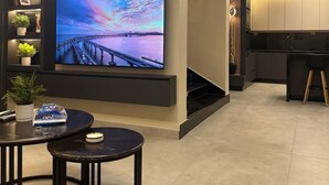 Een moderne woonkamer met een grote flatscreentelevisie, een kleine ronde tafel en een trap naar een keuken.