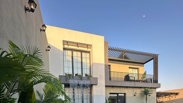 Zwembad met waterval, omringd door weelderige begroeiing en moderne architectuur.