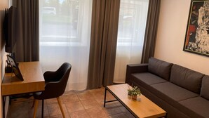 Ein Wohnzimmer mit einer Couch, einem Esstisch mit einem Stuhl, einem Couchtisch mit einer Pflanze und einem Fernseher auf einem Schrank.