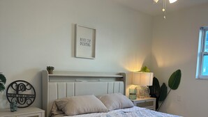 Ein Schlafzimmer mit einem Bett, einem Nachttisch, einem Deckenventilator, einer Wandleuchte und einem Fenster.