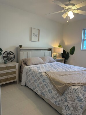 Et soveværelse med seng, et natbord, en loftsvifte, vægmonteret lampe og et vindue.