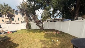 Ein Garten mit weißem Zaun, einem Baum und vereinzelten Gegenständen.