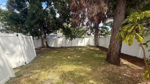 Ein eingezäunter Garten mit Gras, Bäumen und einem weißen Zaun.