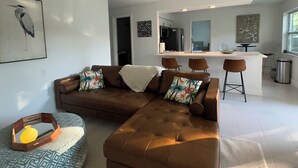 Ein modernes Wohnzimmer mit einer Eckcouch, einem Essbereich mit Barhocker und einer Küche im Hintergrund.