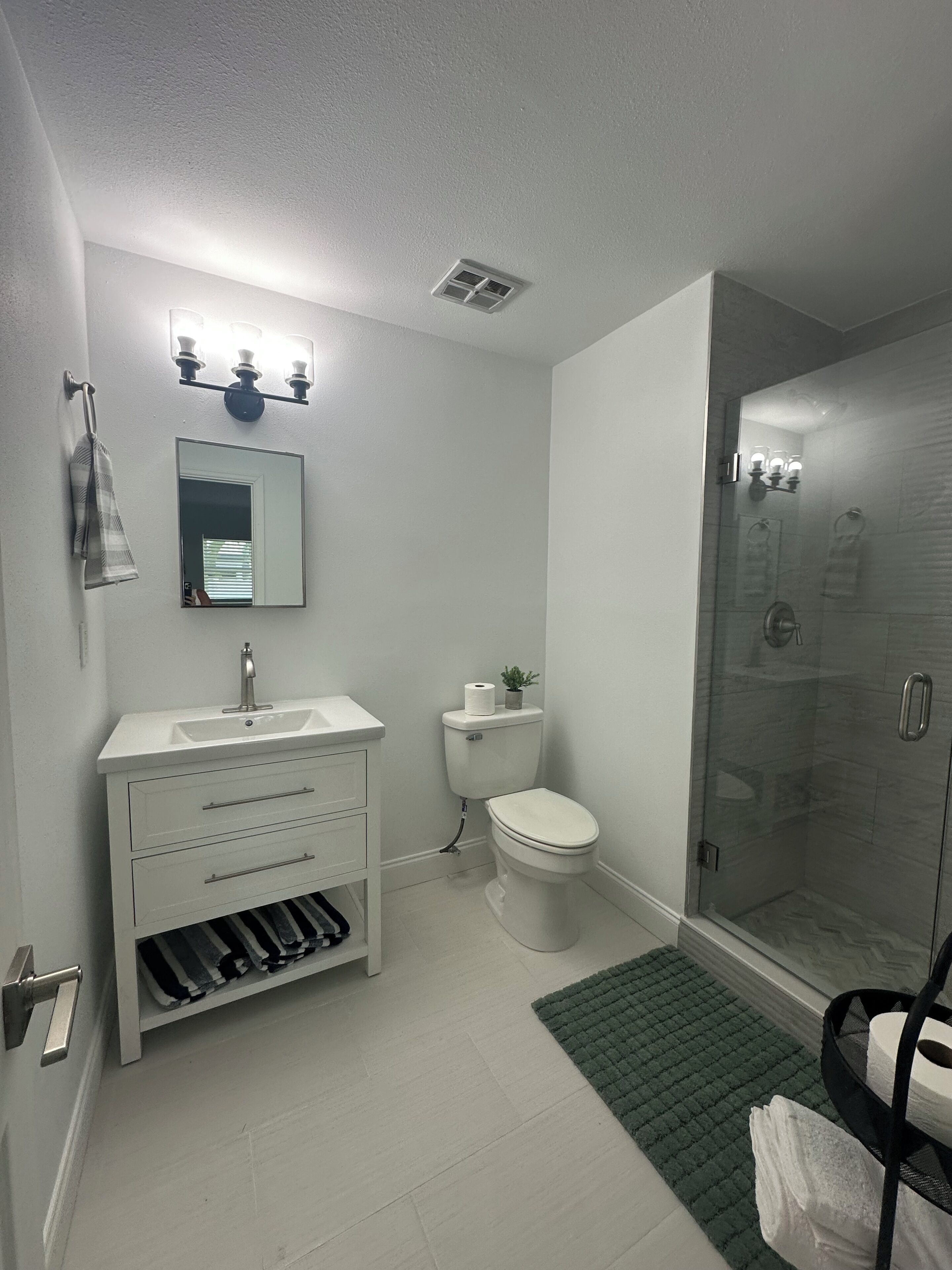 Et badeværelse med toilet, vask, spejl og brusebad.
