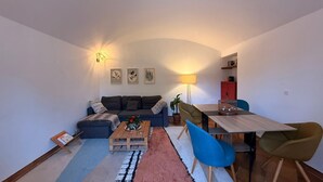 Un salon comprenant un canapé, une table basse et des fauteuils, une table à manger avec des chaises, une lampe et des œuvres d’art murales.