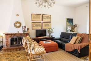 Ein Wohnzimmer mit Kamin, einer Couch, einem Fernseher und gerahmten Kunstwerken an der Wand.