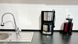 A kitchen with a sink, a coffee maker, and a drawer with utensils.