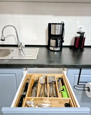 Eine Küche mit Spüle, Kaffeemaschine und einer Schublade voller Besteck.