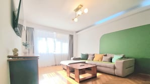 A living room with a sofa, a coffee table, a flat-screen TV mounted on the wall, and a green accent wall.