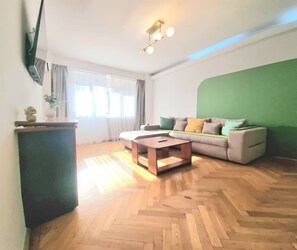 Ein Wohnzimmer mit einer Couch, einem Couchtisch, einem an der Wand montierten Flachbildfernseher und einer Wand in Grünton.