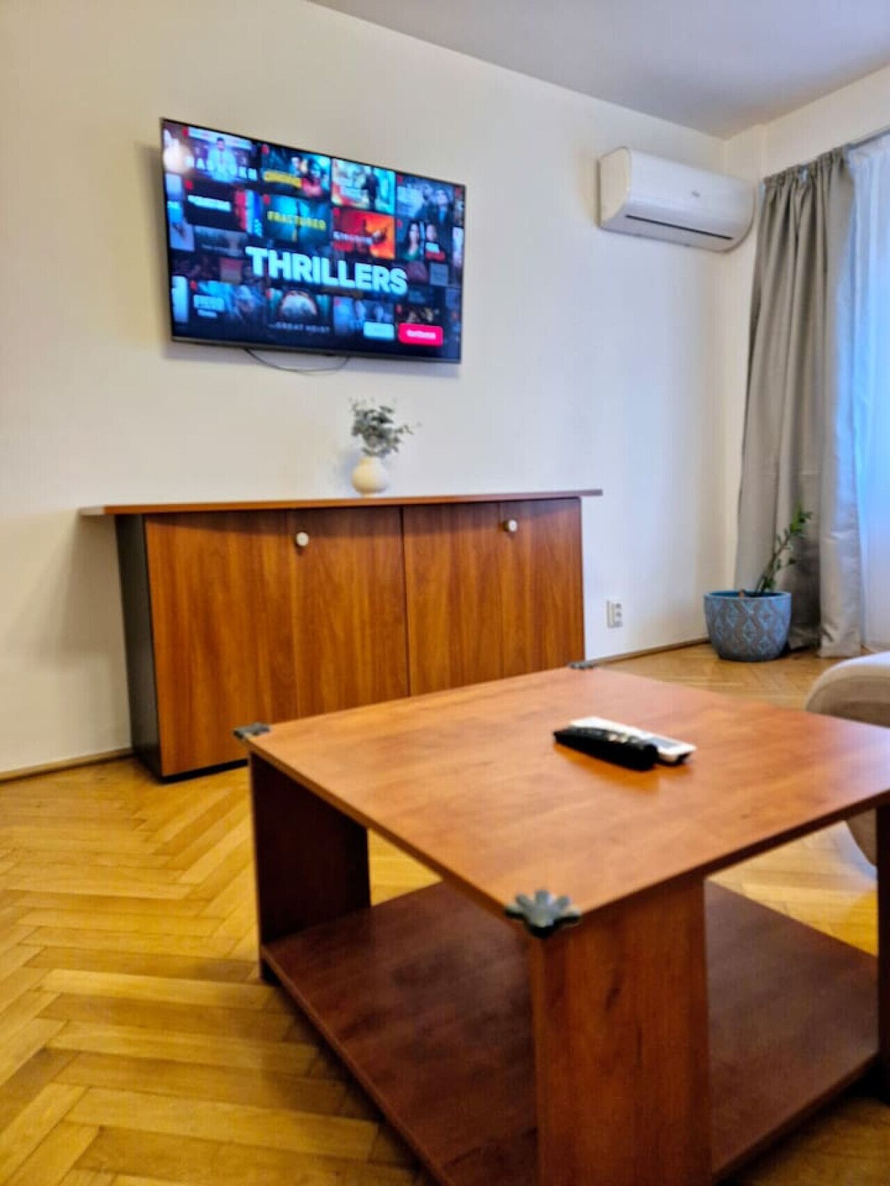 Ein Wohnzimmer mit einem Couchtisch aus Holz, einem an der Wand montierten Fernseher, einem Schrank und einer Klimaanlage.