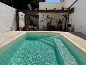 A swimming pool with a wooden pergola, a dining area with chairs and a table, and a wall decorated with various items. - Adorable little villa in the center of Santa Maria di Leuca (Santa Maria di Leuca)
