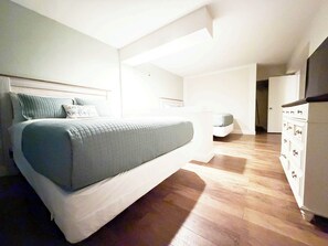 Une chambre à coucher comprenant un lit, une commode et une porte donnant sur une autre pièce.