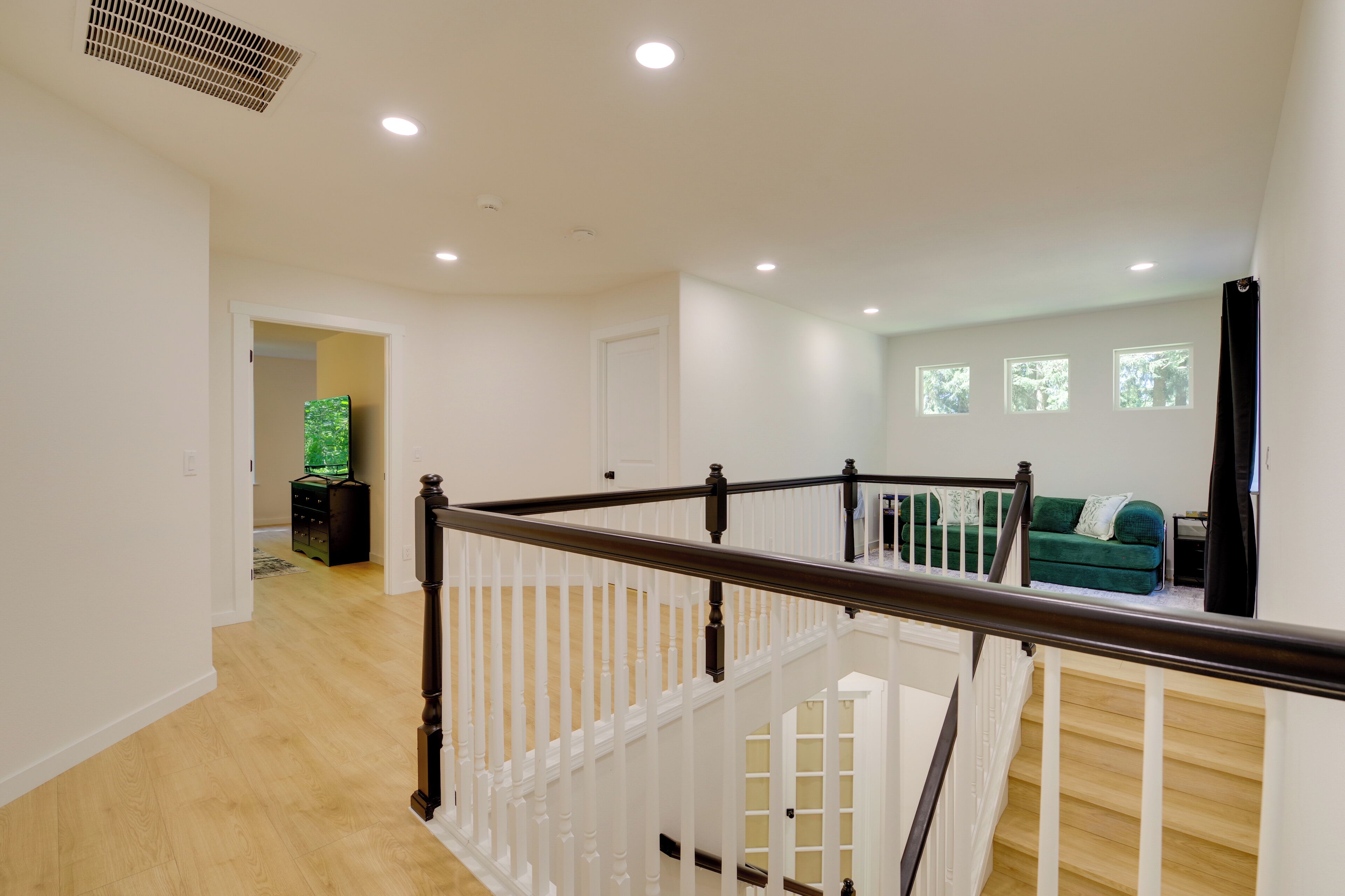 Un interior espacioso con una escalera de madera, un sofá verde y un televisor de pantalla plana en un pasillo.