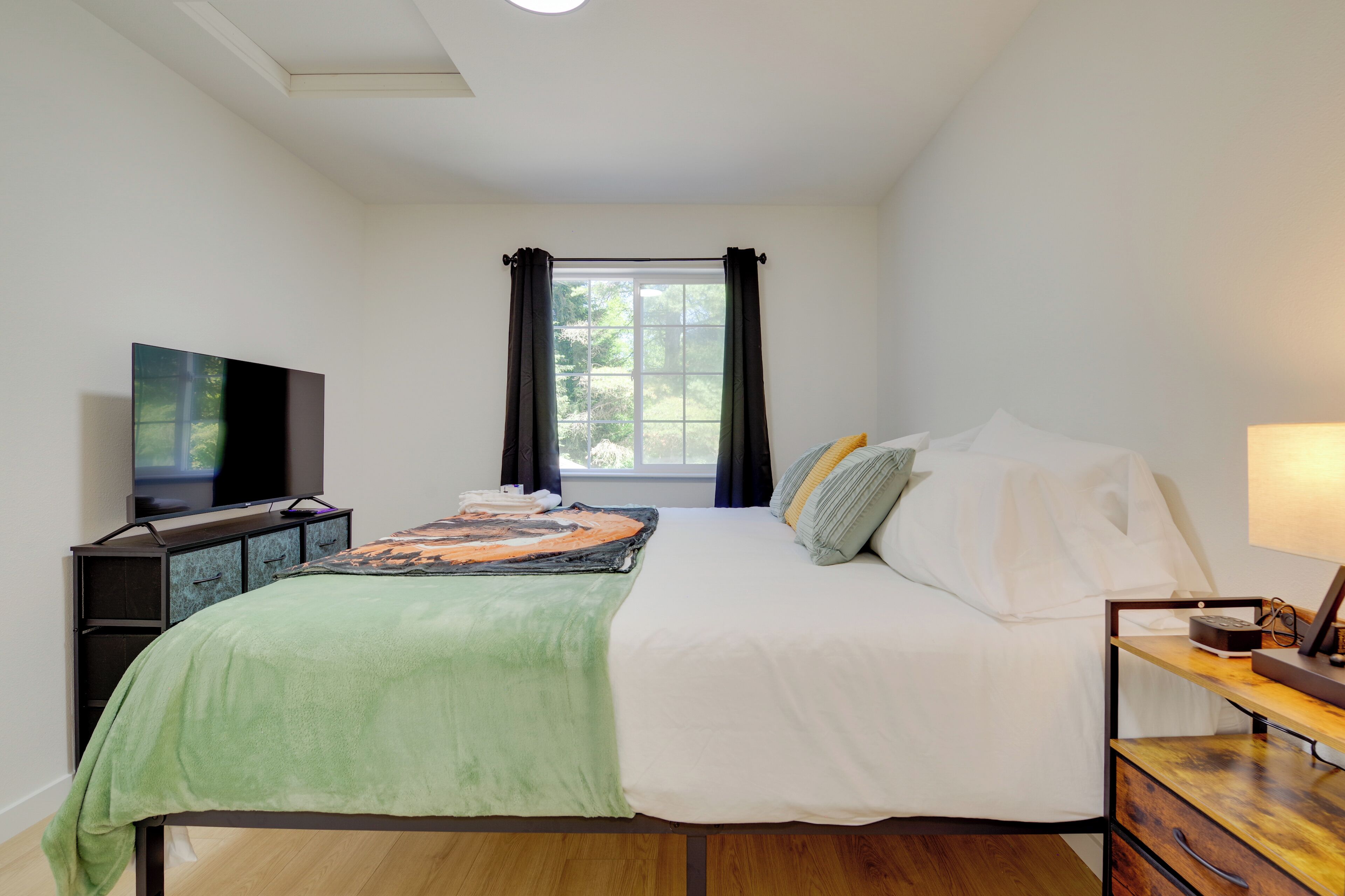 A bedroom with a bed, a TV, a desk, and a window with curtains.