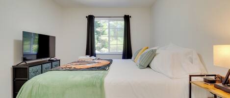 A bedroom with a bed, a TV, a desk, and a window with curtains.