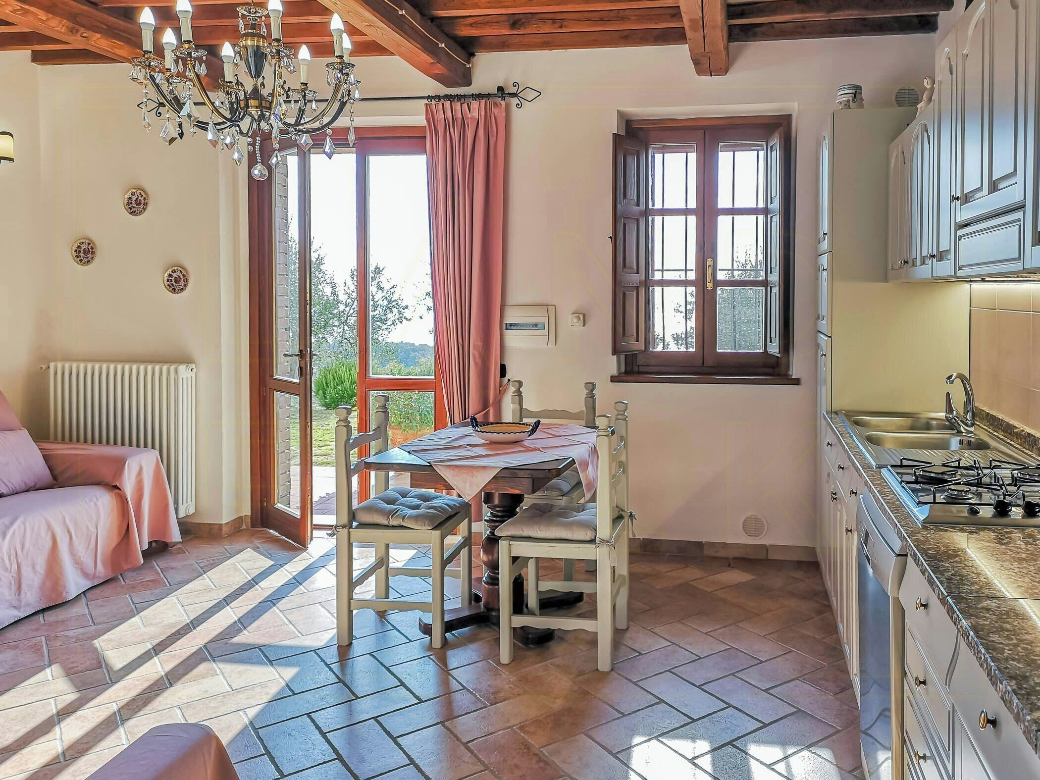 Une cuisine chaleureuse avec une table à manger, des chaises, un lustre et une vue par la fenêtre.