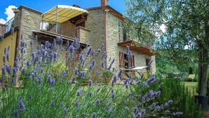 A stone house with a balcony, surrounded by lavender plants. - Umbrian Hillside House with Stunning Views (Lisciano Niccone)