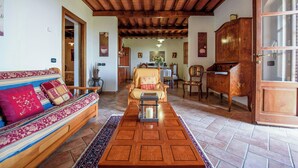 A living room with a wooden ceiling, a sofa with patterned cushions, a coffee table, and a cabinet. - Umbrian Hillside House with Stunning Views (Lisciano Niccone)