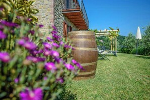 Ein Steingebäude mit einem Holzfass, einer Pergola und einem Rasen.