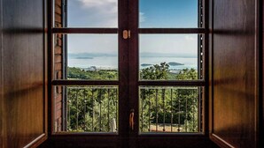 A room with a large window offering a view of a forested area and distant mountains. - Umbrian Hillside House with Stunning Views (Lisciano Niccone)