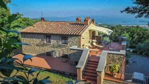 A stone house with a tiled roof, a patio with outdoor furniture, and a view of the sea. - Umbrian Hillside House with Stunning Views (Lisciano Niccone)