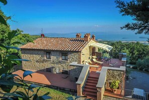 Ein Steinhaus mit einem Ziegeldach, einer Terrasse mit Gartenmöbeln und Blick aufs Meer.