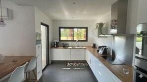 A modern kitchen with white cabinets, a wooden countertop, a built-in oven, and a window with a view of greenery. - Family villa with pool and palm trees, between sea and garrigue (Teyran)
