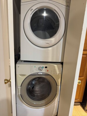 A stacked washer and dryer unit with control panels, a door handle, and a wooden cabinet in the background. - 2-bedroom apartment in fabulous Houston with cool AC (Houston)