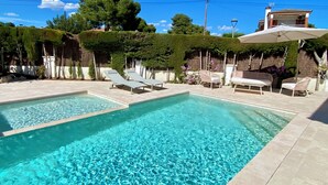Una piscina rectangular con tumbonas y sombrillas, rodeada de vegetación y un cielo despejado.