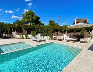 A rectangular swimming pool with lounge chairs and umbrellas, surrounded by greenery and a clear sky. - New Valparaiso house with private pool 8 people (Cunit)