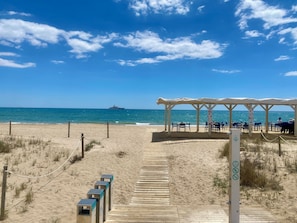 A beach with a wooden walkway, a covered seating area, and a pier with a ship in the distance. - New Valparaiso house with private pool 8 people (Cunit)