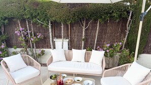 Un patio con un sofá de mimbre blanco, dos sillones blancos y una mesita con comida y bebidas.