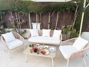 A patio with a white wicker sofa, two white armchairs, and a small table with food and drinks. - New Valparaiso house with private pool 8 people (Cunit)