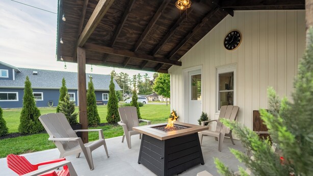 A covered patio with a fire pit, outdoor chairs, and a clock on the wall.