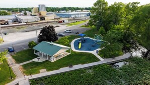 An aerial view of a park with a playground, a small building, and a parking lot.
