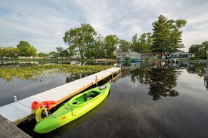 Una masa de agua tranquila con un muelle, un kayak verde y una casa al fondo.