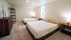 A bedroom with two beds, a wooden dresser, a metal drying rack, and a window with natural light.