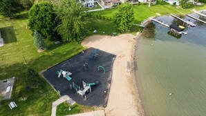 An aerial view of a park with playground equipment, a sandy beach, and a body of water.