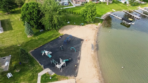 Vista aérea de un parque con juegos infantiles, una playa de arena y una masa de agua.