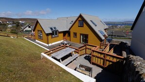 A yellow house with a sloped roof, a wooden deck, and a stone wall.