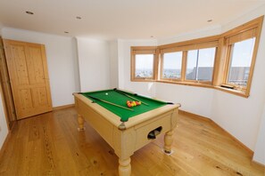 A pool table in a room with wooden flooring, a wooden door, and a window with a view.