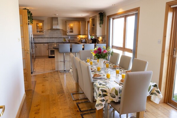 A modern kitchen with wooden cabinets, a dining area with a table set for breakfast, and a view through the window.