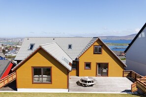 A yellow house with a sloped roof, a wooden deck, and a view of a body of water and distant landscape.