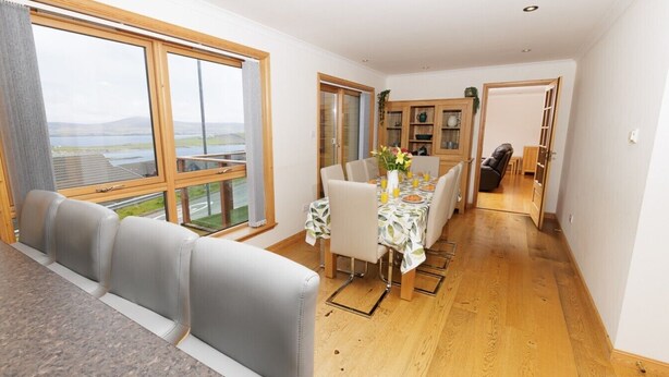 A modern interior with a dining area, a sofa, and a view through large windows.
