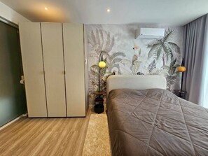 Une chambre à coucher comprenant un lit, une armoire et un mur orné d’une fresque aux motifs tropicaux.