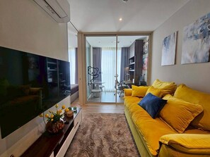 Un salon moderne doté d’un grand téléviseur à écran plat, d’un canapé jaune et d’une porte en verre donnant sur un coin repas.
