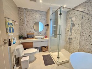 Une salle de bain moderne avec une douche à parois de verre, un miroir rond, un lavabo blanc et des toilettes.