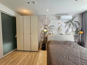 Une chambre à coucher comprenant un lit, une armoire et un mur orné d’une fresque aux motifs tropicaux.
